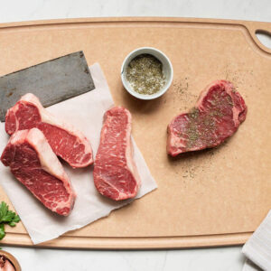 Sage cut board with four steaks and a knife.