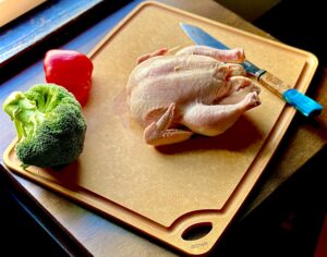 Overhead picture of Sage carving board with whole turkey, knife, pepper, and broccoli on top